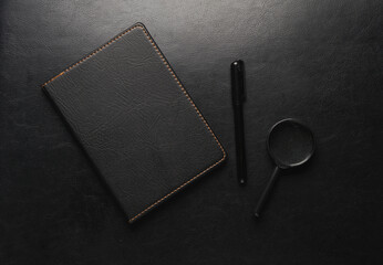 Poster - Black leather notebook with pen and magnifying glass on leather surface.