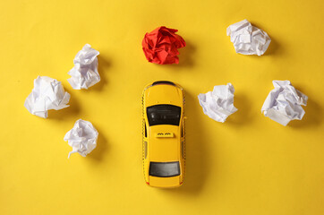 Toy taxi car model with crumpled balls of paper on yellow background. Top view