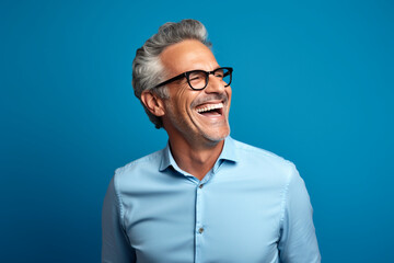 Wall Mural - Portrait of a happy mature man in eyeglasses laughing on against blue background. 