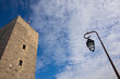 A tower and a streetlamp with a cloudy blue sky on the background.