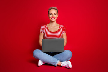 Wall Mural - Photo of adorable lovely girl wear stylish clothes sitting floor using modern gadget isolated on red color background