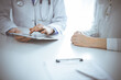 © rogerphoto - Doctor and patient sitting near each other at the desk in clinic. The focus is on female physician's hands pointing into tablet computer touchpad, close up. Medicine concept