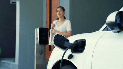 Wall Mural - A woman unplugs the electric vehicle's charger at his residence. Concept of the use of electric vehicles in a progressive lifestyle contributes to a clean and healthy environment.