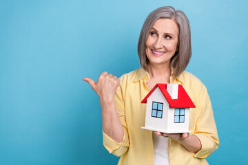 Sticker - Portrait of attractive person hold small house look direct finger empty space ad isolated on blue color background