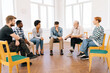 © dikushin - Wide shot of bearded aged professional male mentor leader counselor coach speaking at diverse business meeting with team people or patients group, during training psychotherapy session.