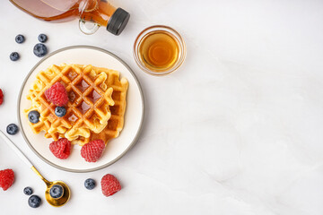 Wall Mural - Plate of tasty waffles with berries and maple syrup on white background