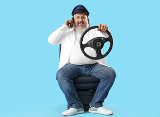 Poster - Mature taxi driver with steering wheel talking by mobile phone on blue background