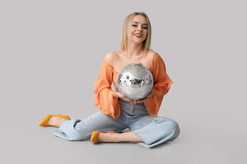 Poster - Beautiful young woman with disco ball sitting on grey background