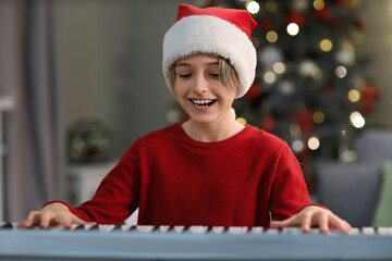 Sticker - Cute little boy in Santa hat playing synthesizer at home on Christmas eve