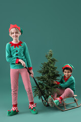 Sticker - Cute little children in elves costumes with Christmas tree and sledge on green background