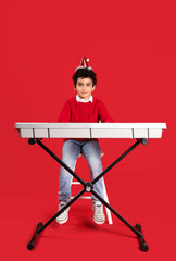 Sticker - Cute little boy in Santa hat playing synthesizer on red background