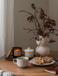Cup of tea, muffins, cranberry branches in a vase, a notebook, a burning candle on a round wooden table in the living room