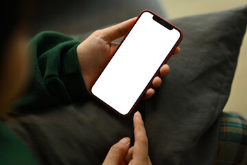 Young woman in green sweater using mobile phone while sitting on sofa. Empty screen for advertising text message