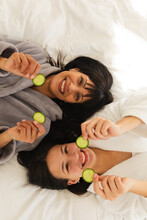 Diverse Mother And Daughter In Bathrobes, Lying On Bed With Cucumber Slices At Home, Copy Space