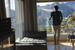 © Wavebreak Media - Rear view of african american man admiring mountain view from living room window, copy space