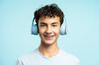 Portrait of attractive smiling boy with dental braces wearing wireless headphones isolated on blue background. Technology, advertisement concept 