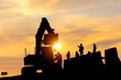 Silhouette of Engineer and worker checking project at building site, Engineer and builders in hardhats discussing on infrastructure construction site sunset in evening time background