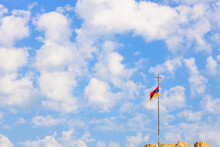 Armenian Flag On Flagpole With Cross On Top Of Hill And Blue Sky With Fluffy White Clouds In Background On Sunny Morning