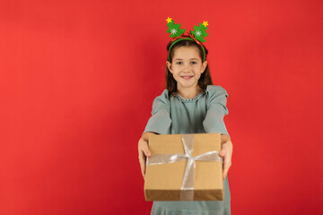 Sticker - Funny teenage girl, christmas decoration on her head, holding a gift on a red background, copy space