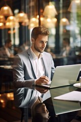 Young businessman works diligently seating at table with laptop in bustling cafe. Man at work online with laptop open on table immersed in professional duties in lively cafe. Vertical photo.