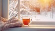 Cozy winter still life: mug of hot tea and warm woolen knitting on vintage windowsill against snow landscape from outside