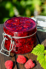 Wall Mural - Red raspberry jam and fresh raspberry on a rustic wooden table outdoors near garden. Rustic style, closeup