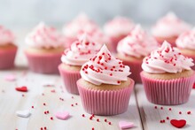 Many Cupcakes With Pink Frosting And Heart Shaped Sprinkles On White Wooden Table