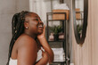 © gstockstudio - Happy plus size African woman radiating self-love while looking at the mirror in domestic bathroom