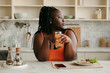 © gstockstudio - Bored plus size African woman holding glass with juice while having lunch at home