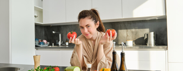 Wall Mural - Portrait of woman cooking at home in the kitchen, holding tomatoes, preparing delicious fresh meal with vegetables, standing near chopping board