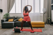© gstockstudio - Full length of beautiful plus size African woman in sportswear looking happy while exercising at home