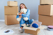 © gorynvd - Beautiful smiling girl puts on the headphones on the teddy bear toy and sitting on the floor in the empty new apartment.