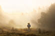 Woman in nature in meadow sunset with mist golden light, back with straw hat, subject in the foreground not in focus