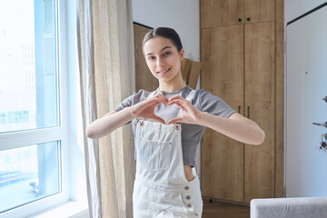 Wall Mural - Teenage girl showing heart sign with hands, smiling looking at camera