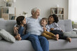 © fizkes - Three multiethnic adorable children boys enjoy conversation with loving hoary great-grandfather, multigenerational family spend weekend time together, having pleasant trustworthy talk in living room