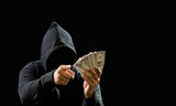 Fototapeta Konie - Portrait bandit man hacker one person wearing hood black shirt, sitting onchair and table thief hand holding money payment counting the amount obtained from hijacking or robbing, in dark background