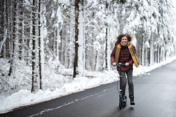 Adult Carefree Caucasian Woman Riding a Kick scooter on Winter Forest Environment Road