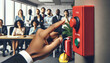 Fire drill. A dark-skinned hand pressing a red fire alarm button, with office workers, safety equipment and  fire extinguisher in background