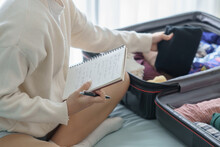 Asian girl preparing vacation in bedroom. Woman doing checklist