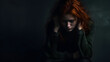 Portrait of a young redhead woman sitting on a floor, hopeless and depressed against a textured, cracked wall.