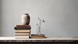 A minimalist composition featuring an earthenware vase, dried plant, and stack of books on a wooden surface against a muted background. Perfect for décor and interior design themes.