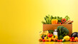 Box full of food in concept delivery and donation box. Cardboard box full of colorful fresh vegetables, fruits and other foodstuffs  on yellow background. No people. Close-up. Copy space.