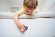 The child is playing alone on the bed and might fall down if not taken care of. Kid aged two years (two-year-old boy)