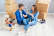 © gorynvd - Couple taking a break on moving day, sitting on floor in new apartment celebrating with champagne surrounded by cardboard boxes.