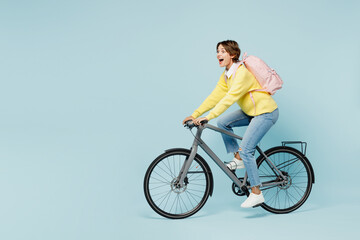 Wall Mural - Full body side view young shocked surprised woman student wears casual clothes sweater backpack bag ride bicycle look aside isolated on plain blue background. High school university college concept.