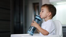 Lovely kid drinking water from a sport bottle. Cute toddler looks at camera, laughs and closes the bottle cap.