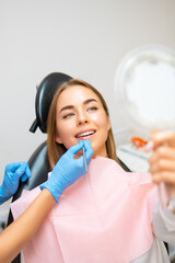 Wall Mural - Woman examines her radiant smile in the mirror after teeth whitening. 