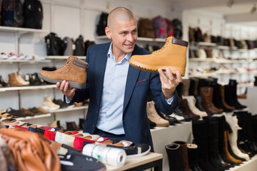 Wall Mural - Portrait of cheerful adult man shopping for mens shoes in store, choosing demi-season lace up boots