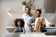 © fizkes - Happy Afro American couple of parents and cute preschooler daughter girl drinking fresh water in kitchen, holding glasses, promoting healthy nutrition, looking at camera, smiling. Home portrait