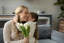 Happy Grateful Mum Holding Flowers, Hugging Sweet Little Daughter Girl With Love, Tenderness, Thanking For Bunch Of Tulips. Kid And Mom Celebrating Mothers Day, Birthday, 8 March